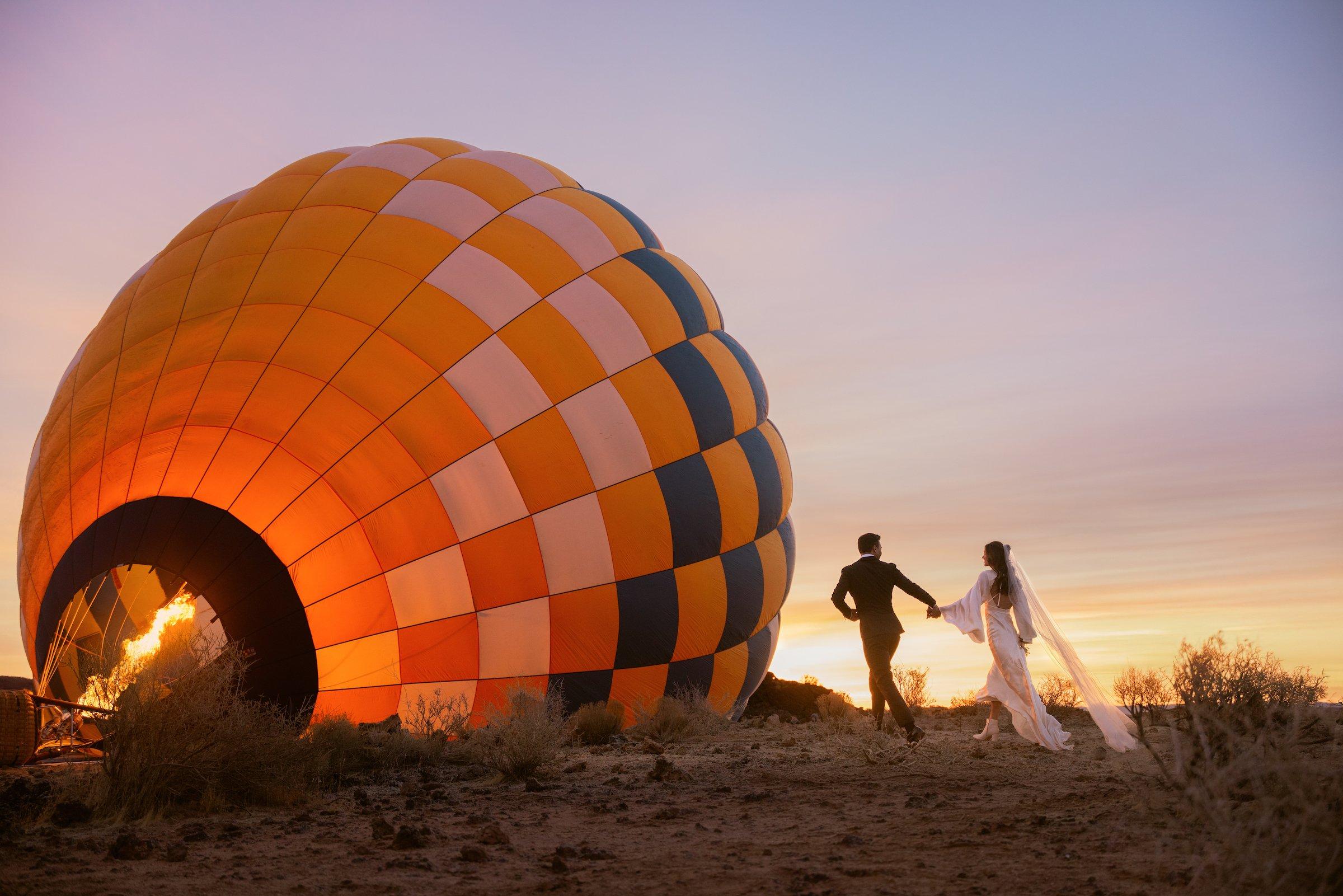 A bride and groom celebrate their destination wedding at Black Desert Resort with a romantic hot air balloon experience at sunset.