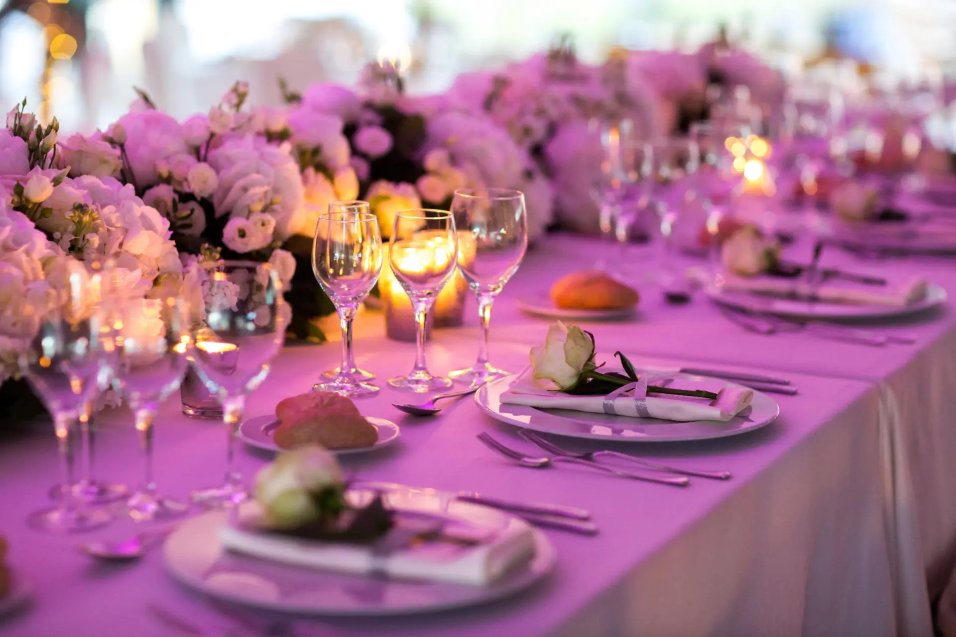 A table set up for a catering event with flowers, wine glasses, plates, utensils, and a purple tablecloth