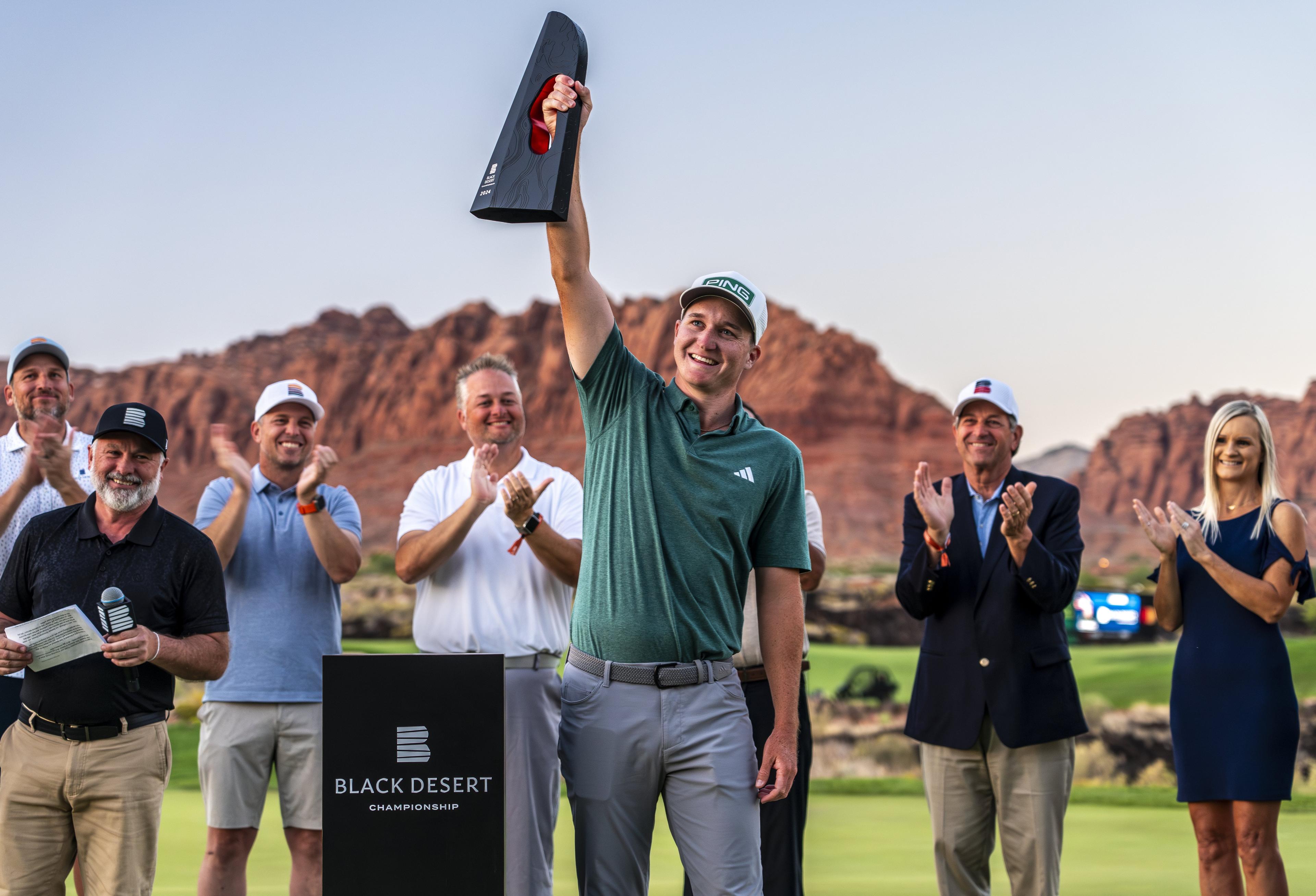 A professional golfer celebrates with the trophy at the awards ceremony for the Black Desert Championship, hosted at Black Desert Resort in Utah.